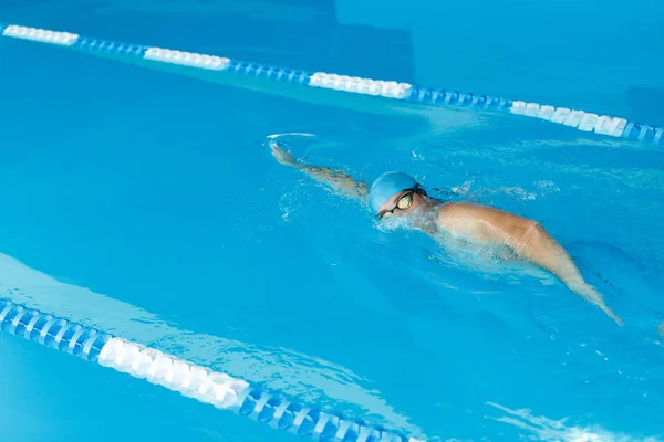 Imagen del atleta hombre en gorra azul nadando bajo el agua en la piscina — Foto de Stock