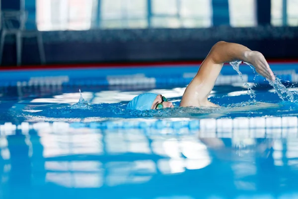 Bild eines jungen Athleten mit blauer Mütze, der im Pool schwimmt — Stockfoto