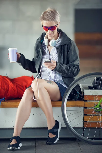 Foto de mujer joven con vidrio sentado en el banco junto a la bicicleta verde —  Fotos de Stock