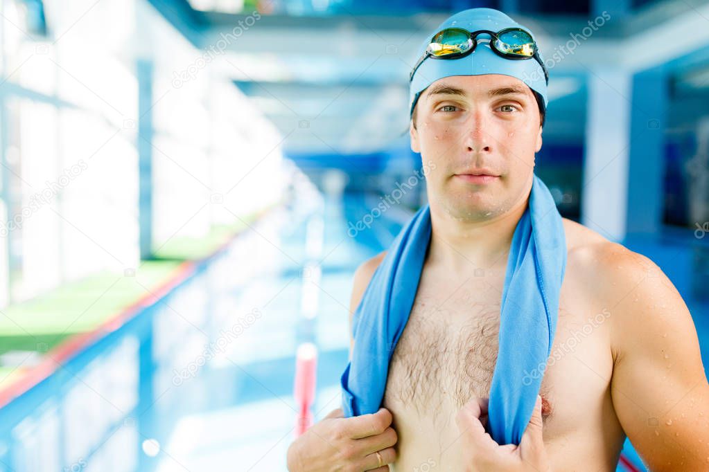 Photo of young swimmer with towel around neck standing in pool during workout