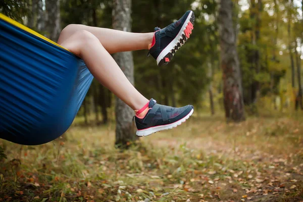 Foto di una donna con le gambe appese in scarpe da ginnastica sdraiata in amaca nel bosco — Foto Stock