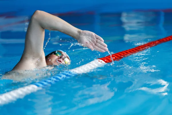 Foto de atleta hombre en gorra azul nadando en la piscina — Foto de Stock