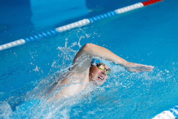 Изображение спортсмена в синей кепке, плавающего в стиле ползания в бассейне
