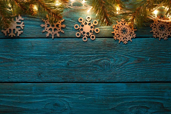 Afbeelding van blauwe houten oppervlak met branden Nieuwjaar garland, sneeuwvlokken, vuren takken. — Stockfoto