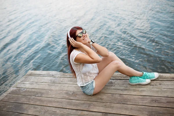 Zdjęcie z brunetka w słuchawki siedzi na drewniany most — Zdjęcie stockowe
