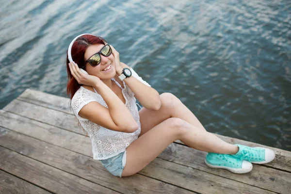Obrázek bruneta v sluchátka sedí na dřevěný most — Stock fotografie
