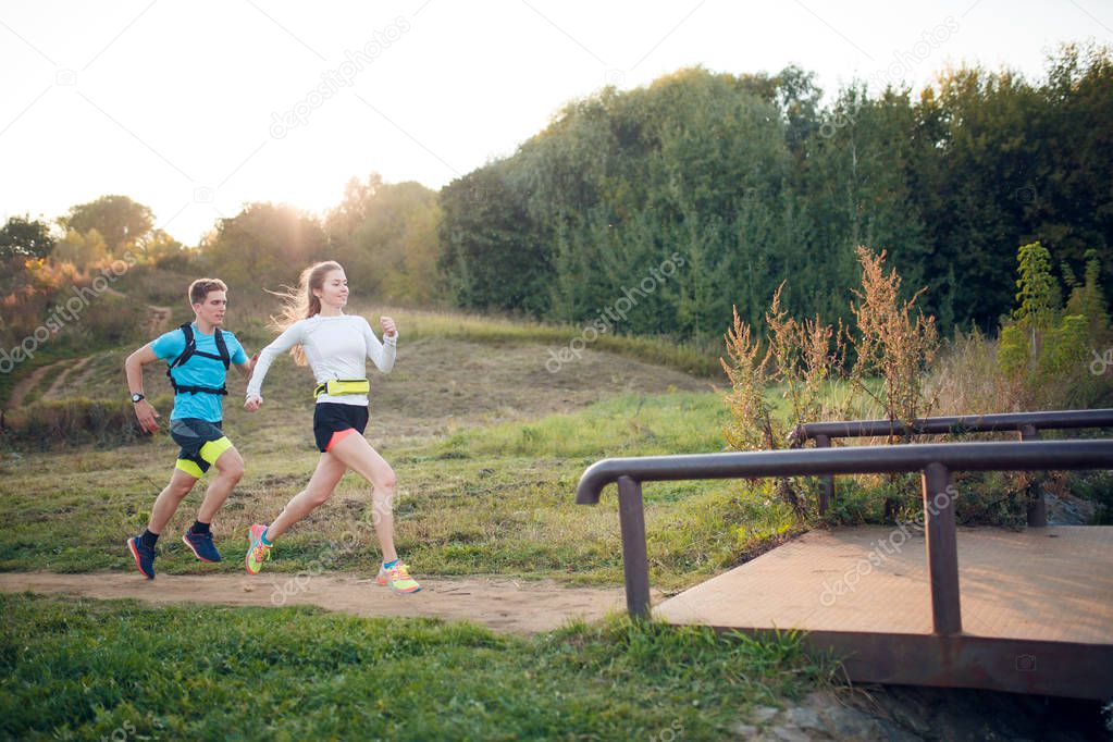 Photo on side of sportive woman and man running through park