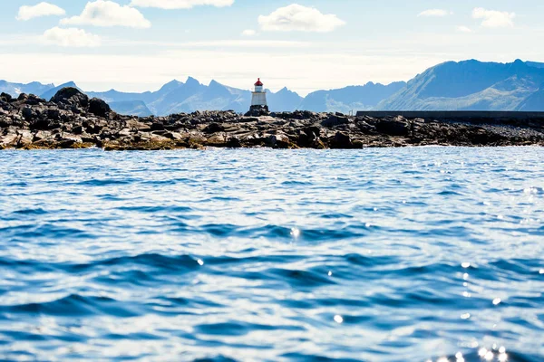 Photo of lighthouse on sea against background of rocks and cloudy blue sky — Stock Photo, Image