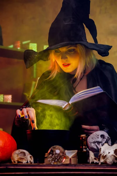 Image de sorcière blonde en chapeau noir avec potion de mise en pot de livre en pot — Photo