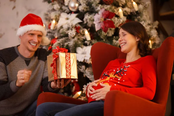 Foto de hombre en Santa cap con regalo y mujer embarazada en árbol de Navidad — Foto de Stock