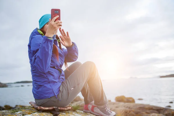 Foto einer Frau auf Stein sitzend mit Handy in der Hand am Meeresufer — Stockfoto