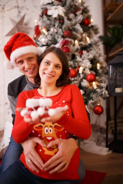 Milující muž a těhotná žena s botičky na pozadí vánočních ozdob — Stock fotografie