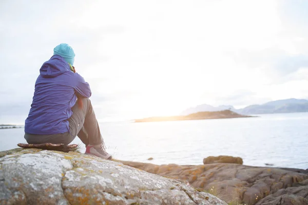 Фото со спины женщины, сидящей на камне у моря — стоковое фото