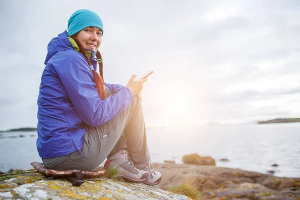 Imagem da mulher sentada em pedra com telefone nas mãos na praia — Fotografia de Stock