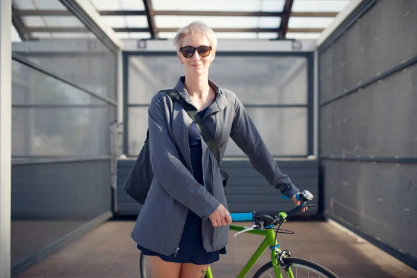 Imagen de mujer rubia en gafas de sol con bicicleta verde contra pared gris —  Fotos de Stock