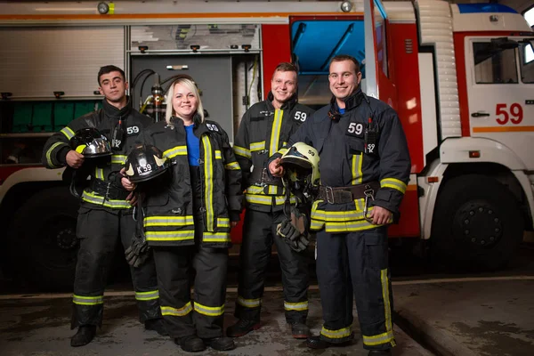 Fullängds foto av tre leende brand män och en kvinna på bakgrund av brandbil — Stockfoto