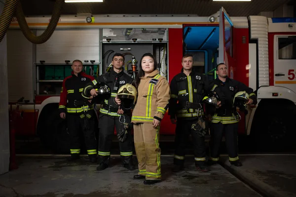 Foto von vier Feuerwehrmännern und -frauen vor dem Hintergrund eines Feuerwehrfahrzeugs — Stockfoto