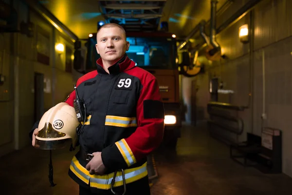 Imagen del bombero sosteniendo el casco en las manos sobre el fondo del camión de bomberos — Foto de Stock