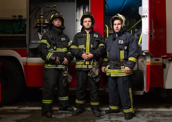 Полнометражное фото трех пожарных на фоне пожарной машины — стоковое фото