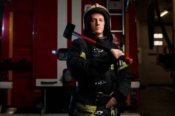 Foto eines Feuerwehrmannes mit Schutzhelm und Hammer auf dem Hintergrund eines Feuerwehrfahrzeugs am Bahnhof — Stockfoto