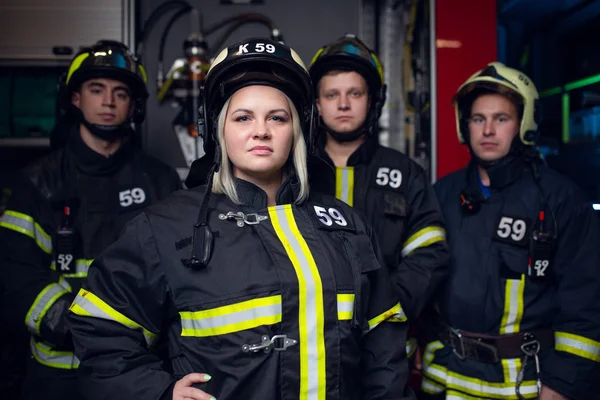 Foto von drei jungen Feuerwehrmännern und -frau vor dem Hintergrund eines Feuerwehrfahrzeugs — Stockfoto