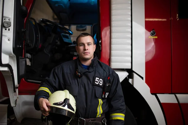 Fotografie člověka hasič s helmou v ruce proti pozadí hasičský vůz — Stock fotografie