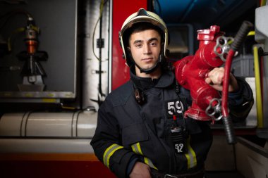 Photo of young man firefighter with fire cock on shoulder against background of fire truck clipart