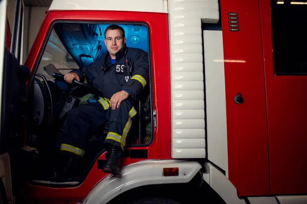 Mladý hasič muž sedící v hasičské auto — Stock fotografie