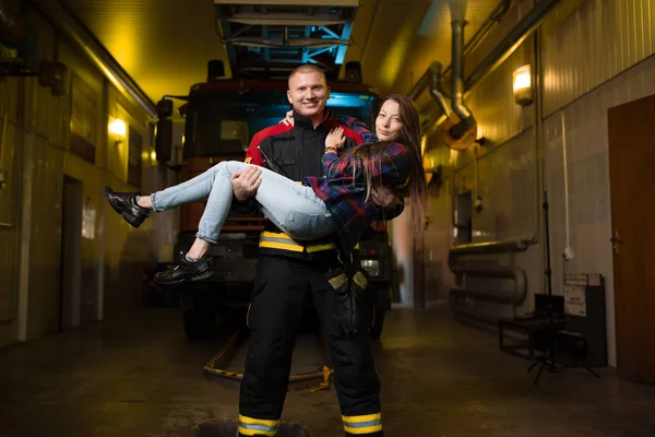 Foto completa de bombeiro segurando mulher em armas no fundo do caminhão de bombeiros — Fotografia de Stock