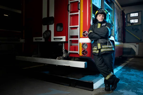 Foto de cuerpo entero de bombero hombre con brazos cruzados por camión de bomberos — Foto de Stock