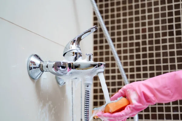 Imagem de mãos em luvas de borracha rosa lavando misturador banheira — Fotografia de Stock