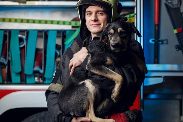 Imagen de bombero joven en casco con perro en el fondo de camión de bomberos — Foto de Stock