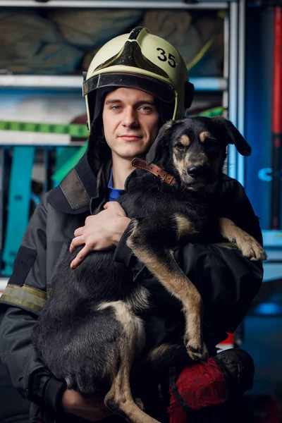 Imagem de bombeiro feliz no capacete com cão no fundo — Fotografia de Stock