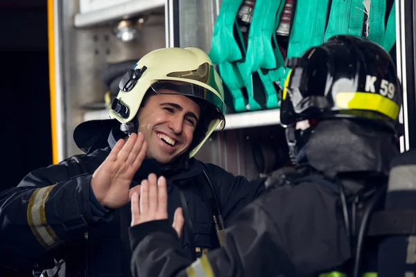 Bild von zwei Feuerwehrmännern beim Händedruck in der Nähe eines Feuerwehrfahrzeugs — Stockfoto