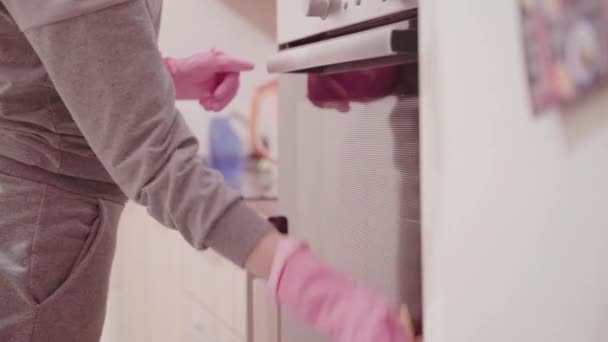 Close-up van jonge vrouw in roze rubberen handschoenen reiniging elektrische oven. — Stockvideo