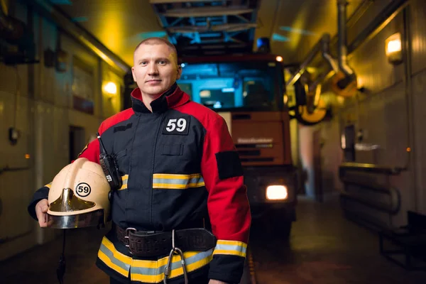 Foto de un bombero sosteniendo el casco en las manos sobre el fondo del camión de bomberos — Foto de Stock