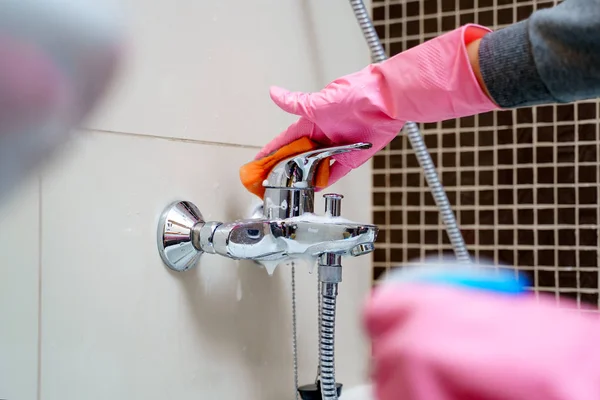 Woman s hand in pink rubber gloves with cleaning agent washing bathtub mixer — Stock Photo, Image