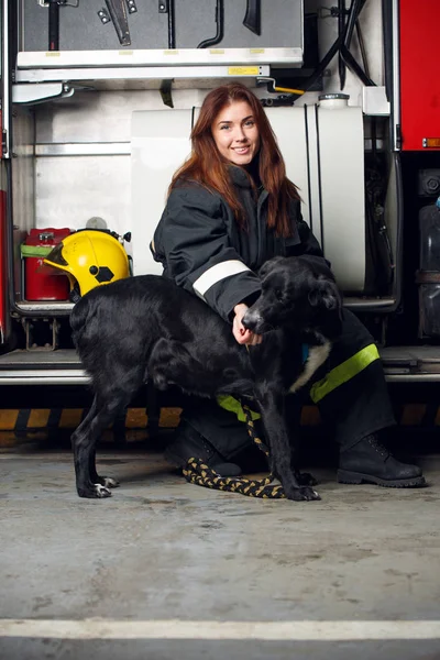 Imagem de mulher bombeira com cão preto sentado no fundo do caminhão de bombeiros — Fotografia de Stock