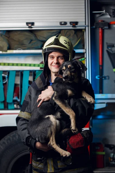 Photo of happy fireman in helmet with dog on background of fire truck — Stock Photo, Image