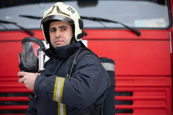 Foto av ung man brandman med mask i händerna nära brandbil — Stockfoto