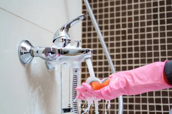 Foto da mão da menina em luvas de borracha rosa lavando misturador banheira — Fotografia de Stock