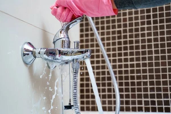 Mano en guantes de goma rosa lavado mezclador de bañera en el baño — Foto de Stock