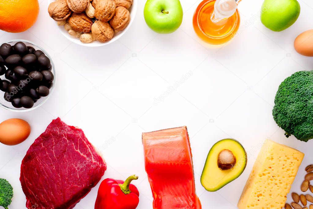 Image on top of piece of meat, fish, cheese, eggs, vegetables, fruits, olives, walnuts on white background.