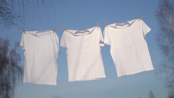 T-shirts suspendus sur la corde à linge contre le ciel bleu — Video