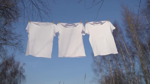 Camisetas colgando en el tendedero contra el cielo azul — Vídeos de Stock