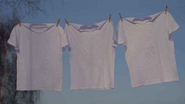 Trička, které visí na prádelní šňůru proti modré obloze — Stock video