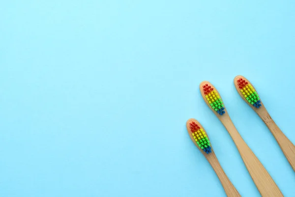 Foto de três escovas de dentes de madeira com cerdas coloridas de arco-íris . — Fotografia de Stock