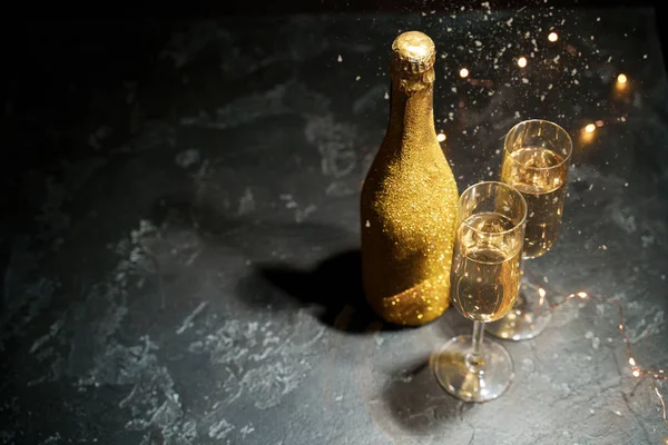 Photo of golden champagne bottle, two wine glasses, burning garlands — Stock Photo, Image