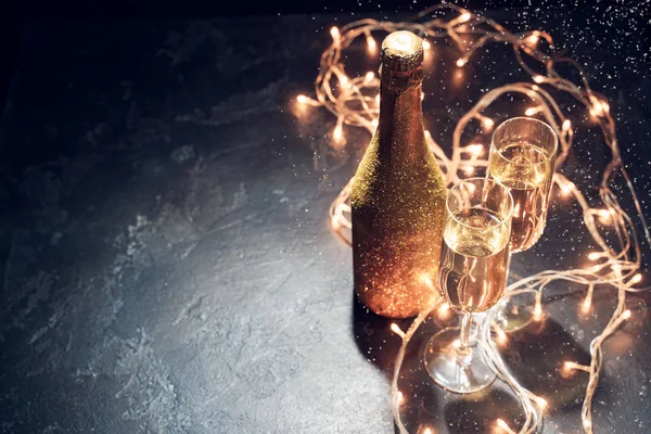 Picture of golden champagne bottle, two wine glasses, burning garlands — Stock Photo, Image