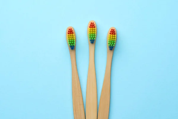 Imagem de três escovas de dentes de madeira com cerdas coloridas de arco-íris . — Fotografia de Stock